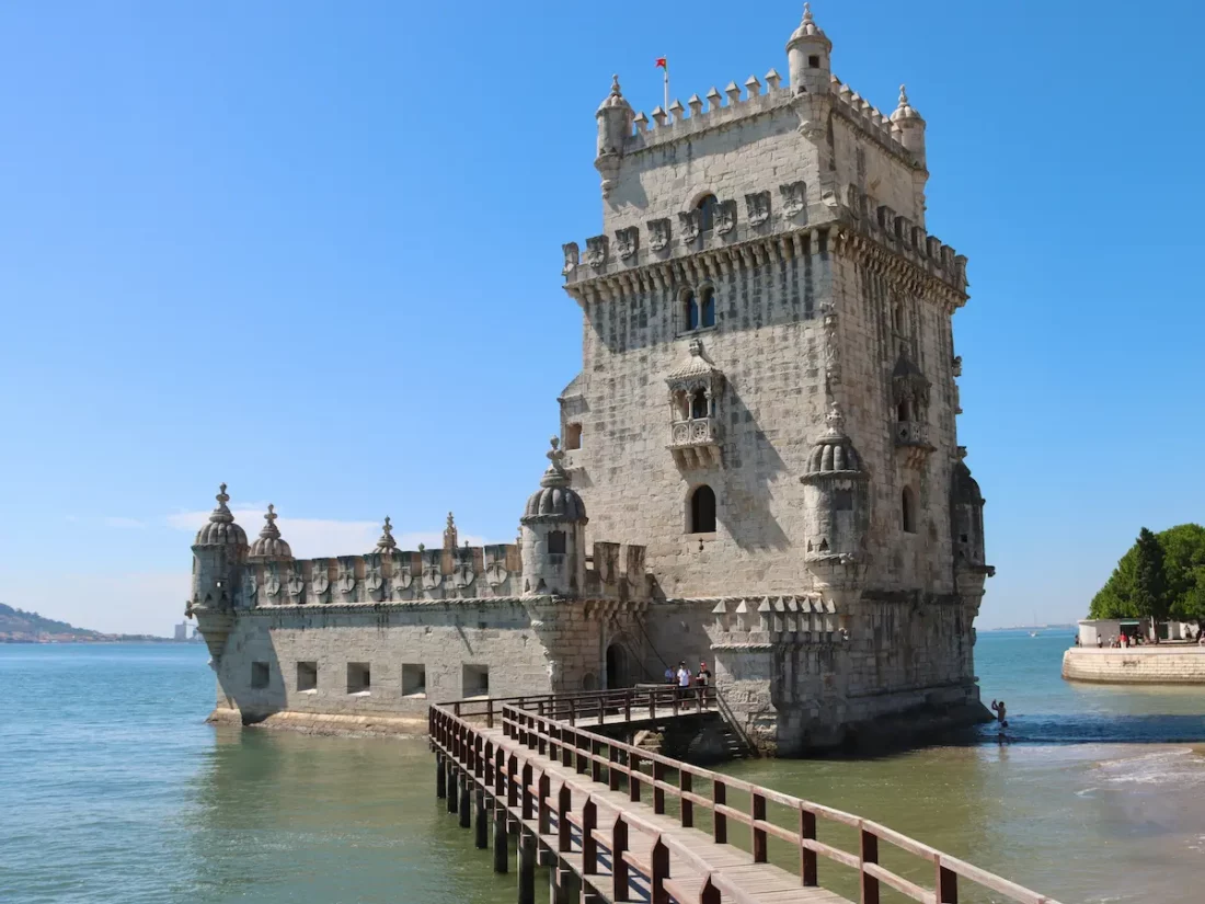 The historic Belém Tower (Torre de Belém) on the banks of the Tagus River in Lisbon under a blue sky.