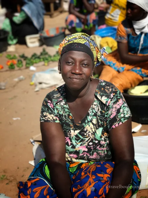 Vrouw met kleurrijke hoofddoek zittend op een lokale markt in Gambia.