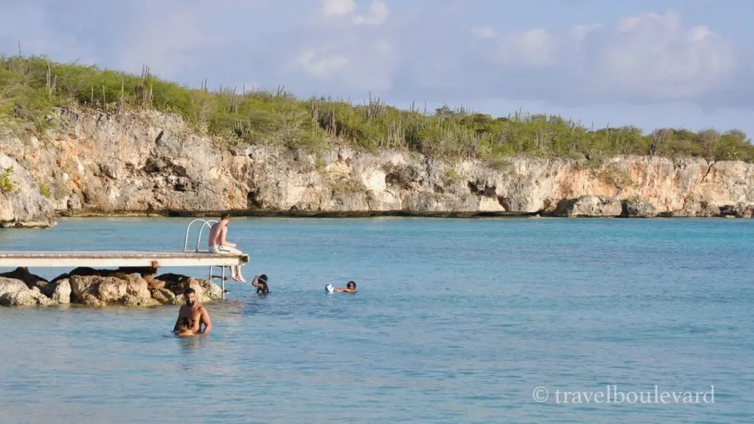 Mensen die zwemmen en zonnen op een houten pier bij de rotsachtige kust van Porto Mari op Curaçao.
