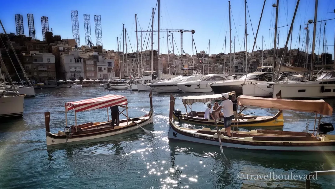 Traditional Maltese dgħajsa boats sailing past luxury yachts in Valletta