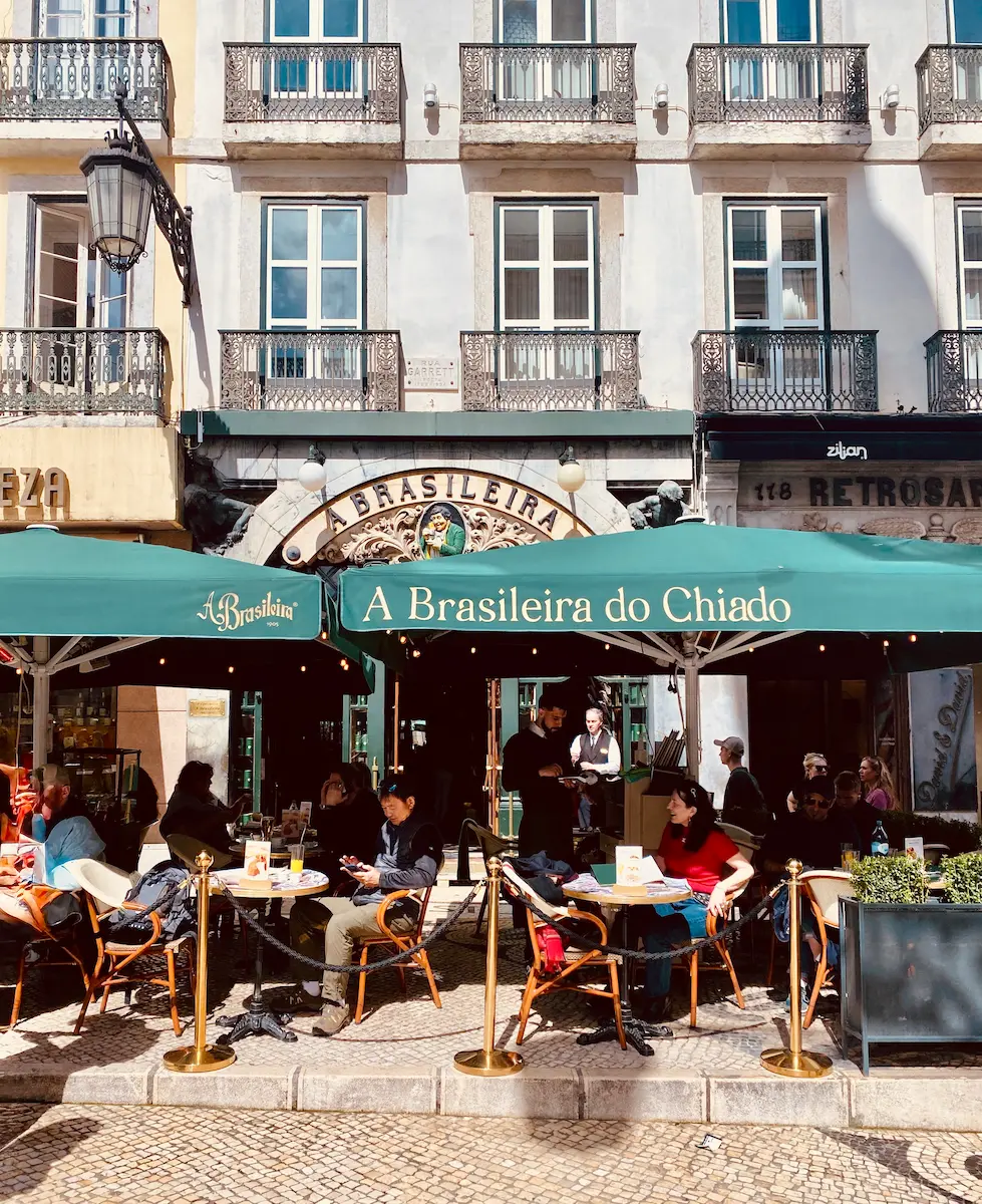 People sitting at the green outdoor tables of the historic café A Brasileira in the Chiado district.
